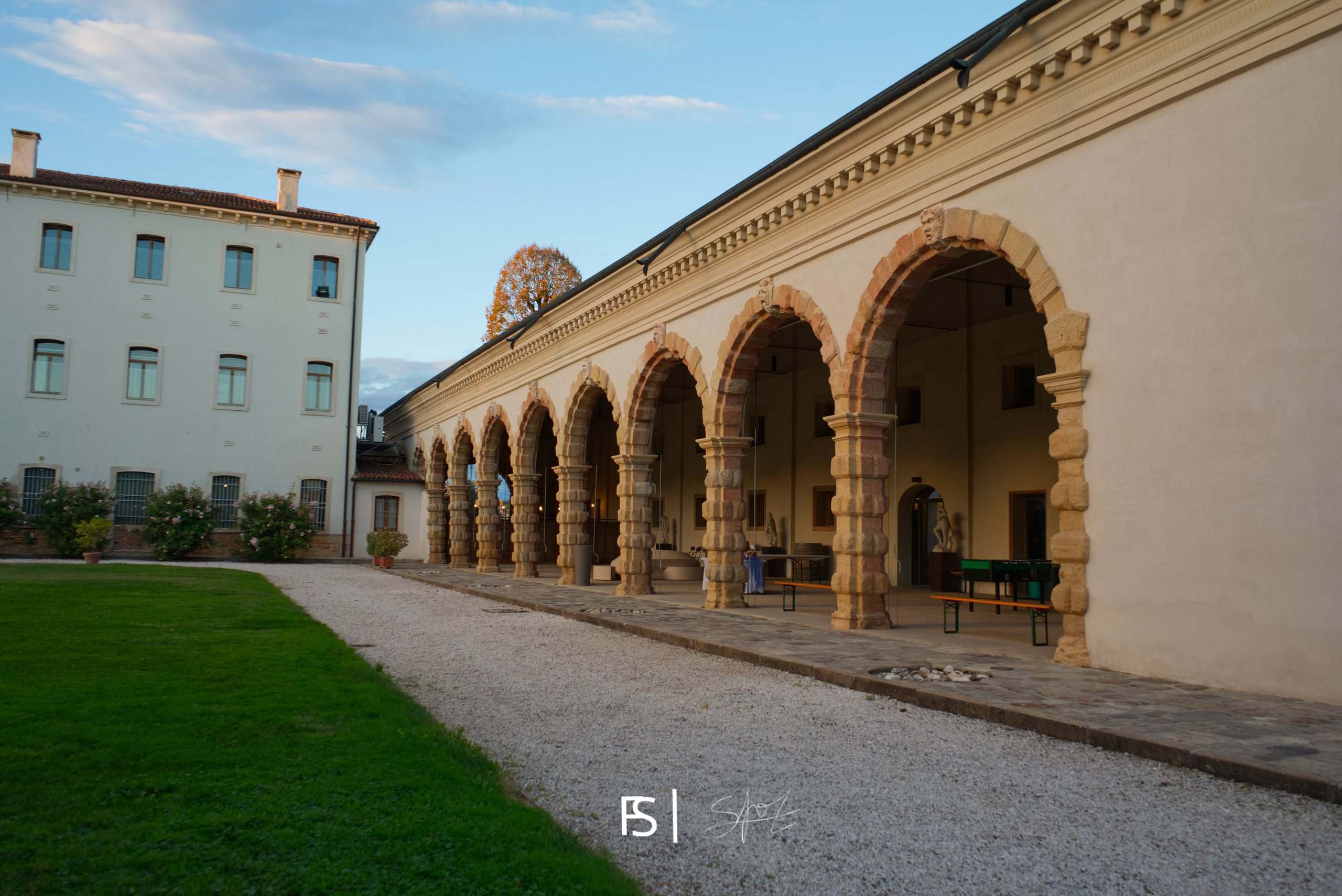 Lungo porticato ad archi in pietra illuminato dal sole del tardo pomeriggio