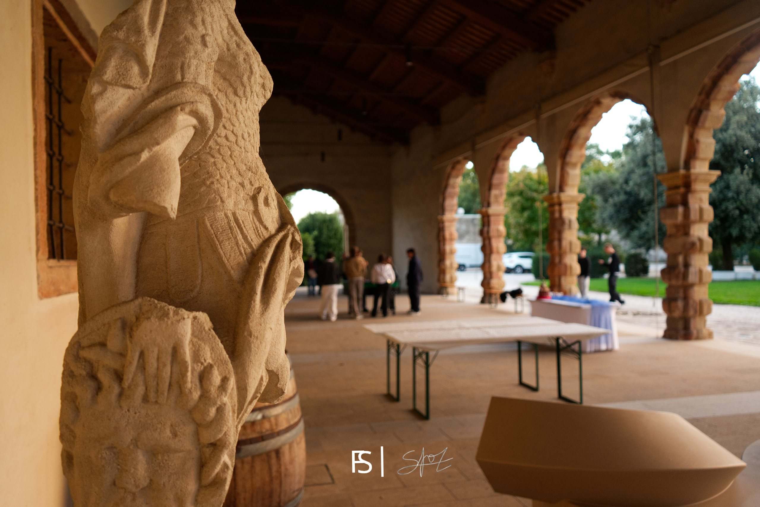 Statua in pietra in primo piano, sullo sfondo il porticato con i primi ospiti