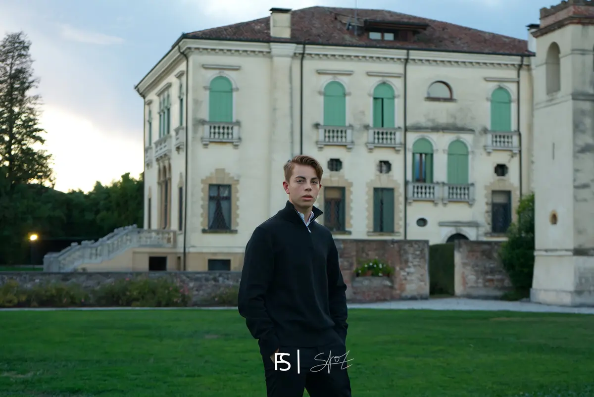 Ritratto del festeggiato in maglione scuro, in piedi sul prato davanti alla villa al tramonto