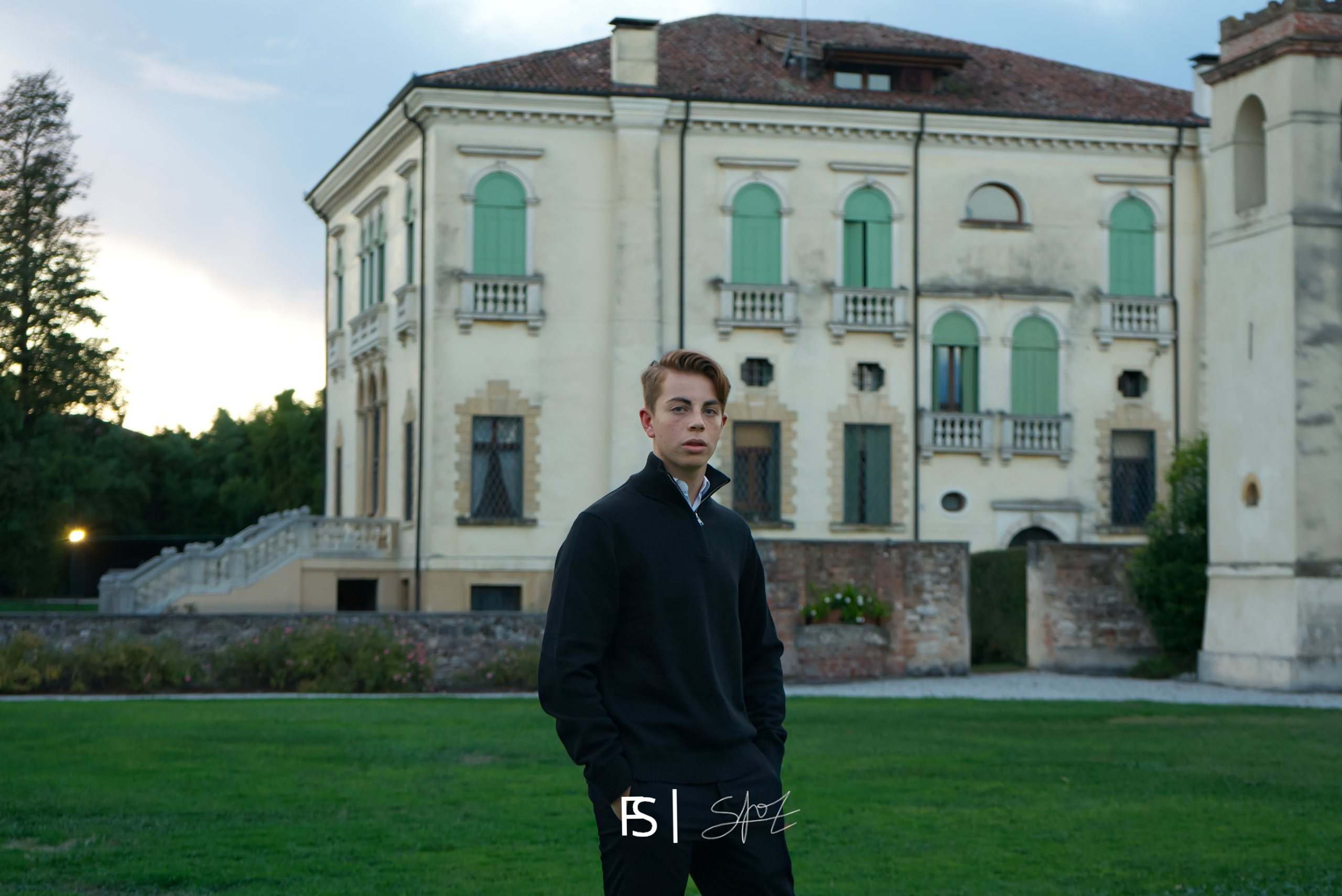 Ritratto del festeggiato in maglione scuro, in piedi sul prato davanti alla villa al tramonto